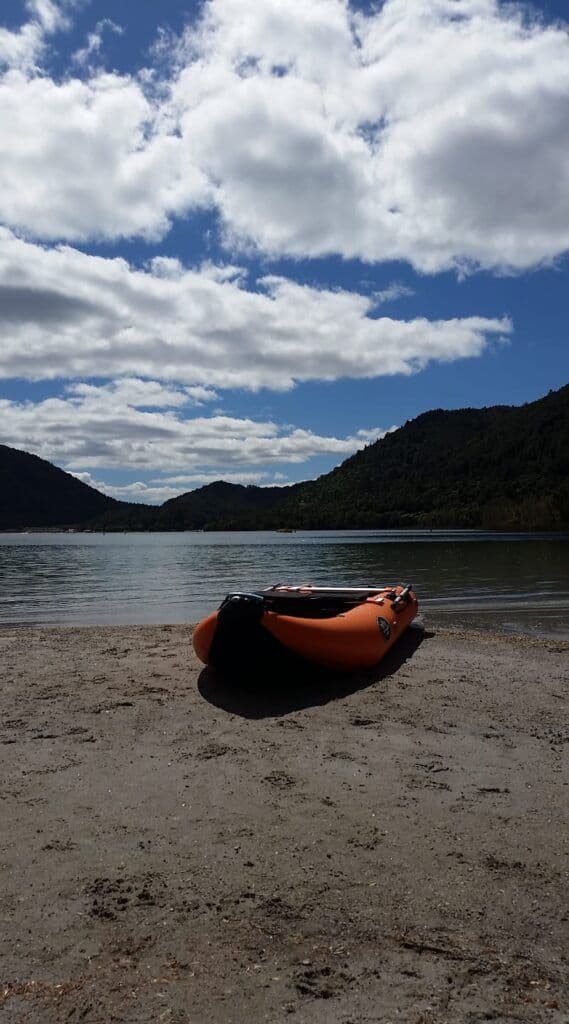 My orange inflatable kayak on shore of the Blue Lake, Rotorua, New Zealand, surrounded by clear water and lush greenery