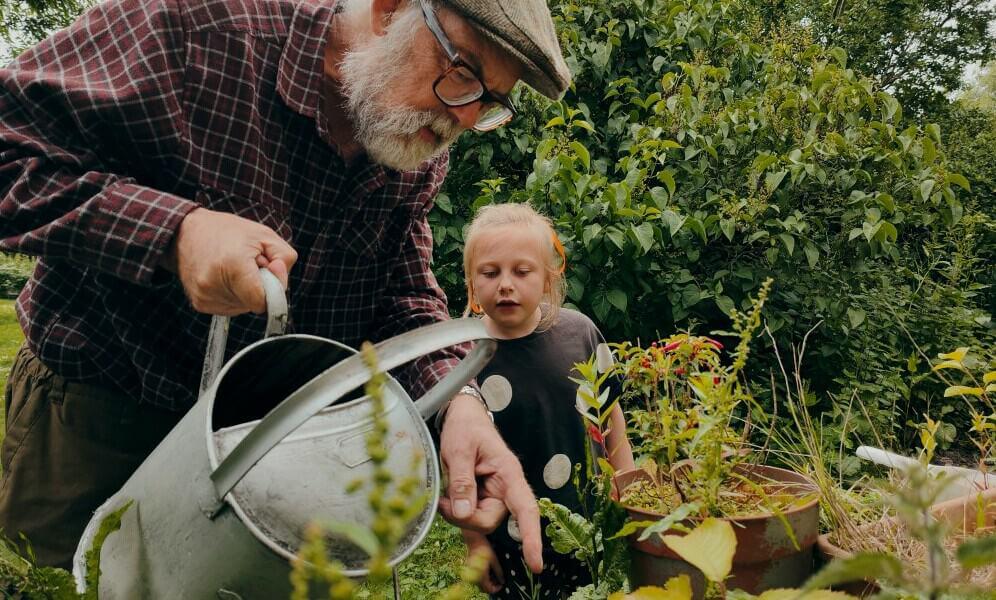 Grandfather showing Granddaughter the garden while he waters with a watering can