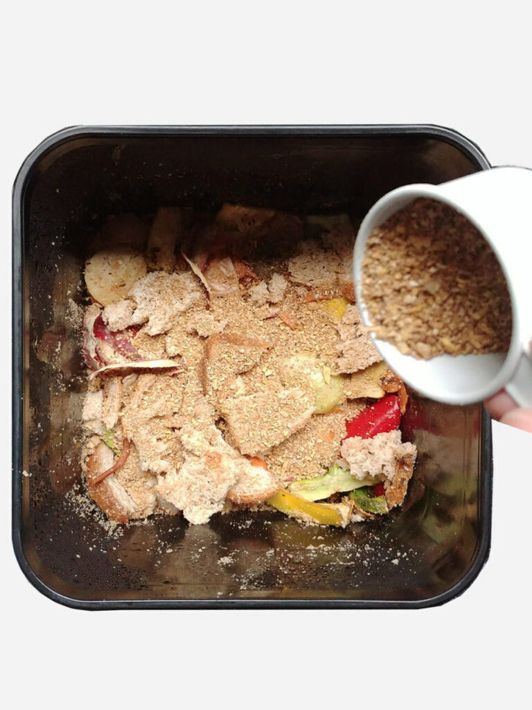 Food scraps inside a container being sprinkled with powder from a cup